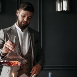 Homme en costume manipulant un décanteur de vin rouge près d’une bougie